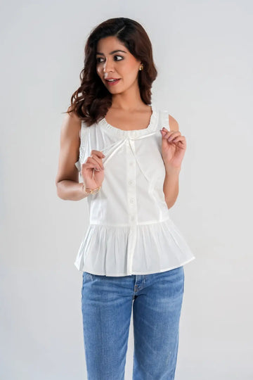 Model holding tie-front accent with hand on white sleeveless cotton cottagecore peplum, featuring frill neckline – feminine summer outfit