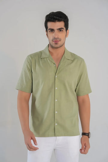 Man wearing a light green shirt and white pants against a plain background