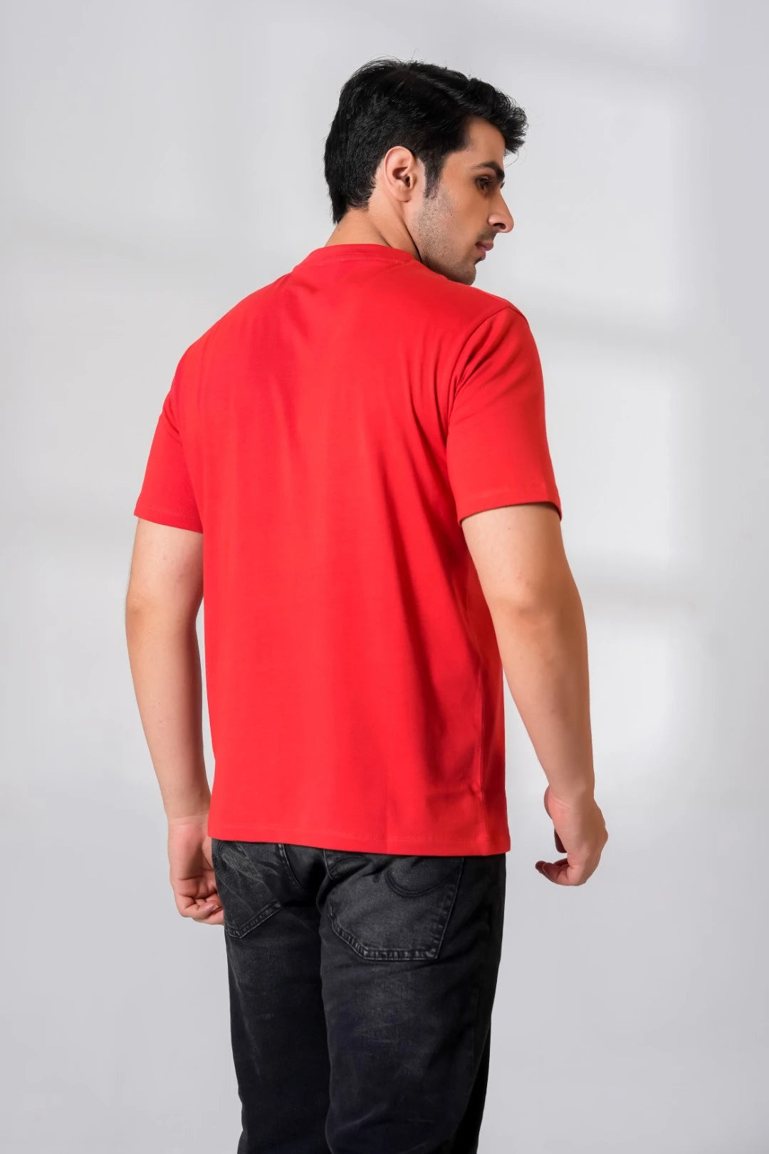 Back view of man wearing a plain crimson red short sleeve t-shirt, paired with black jeans, showing fabric texture and relaxed fit