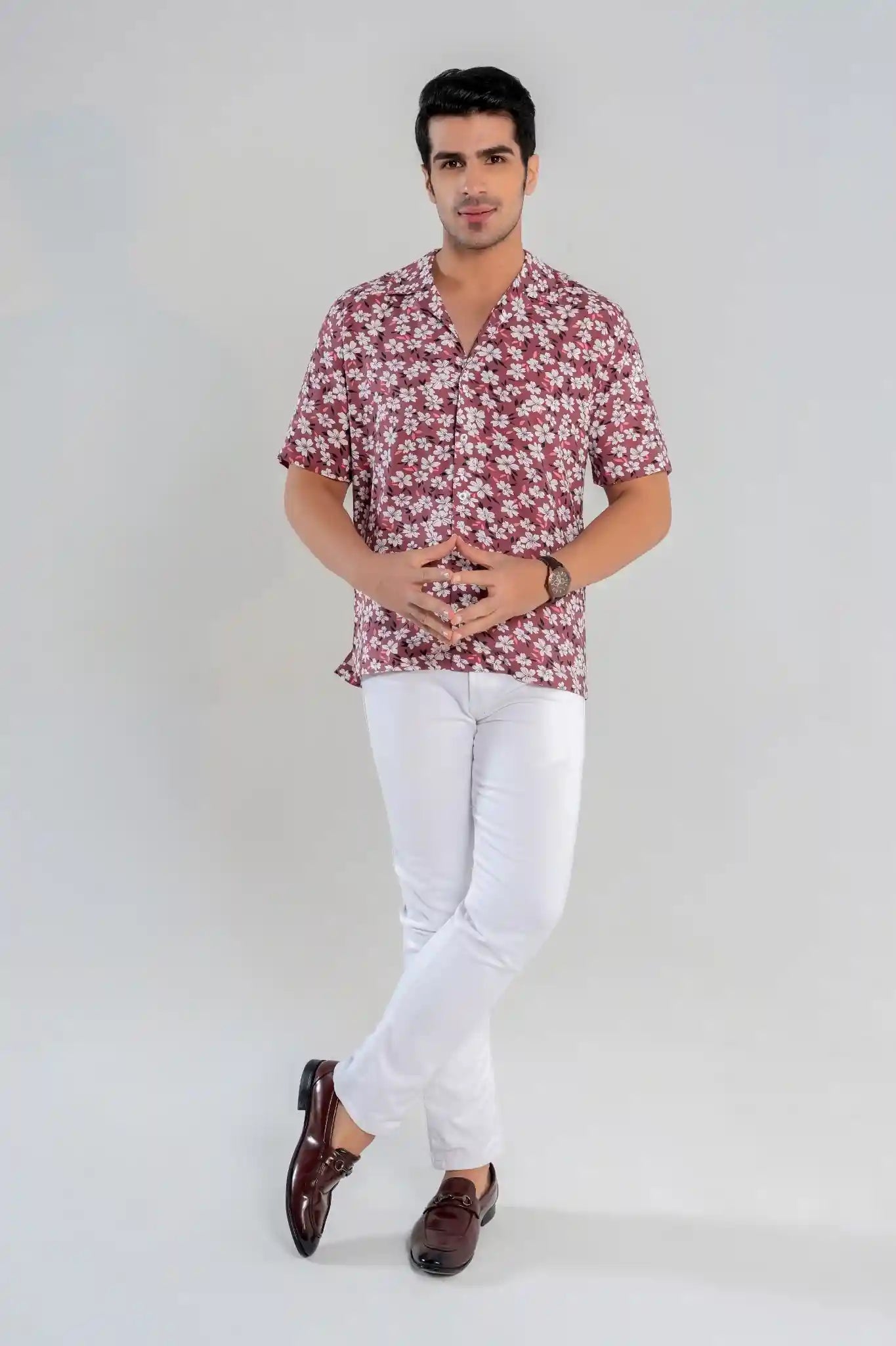 Man wearing a rust floral shirt and white pants on a plain background