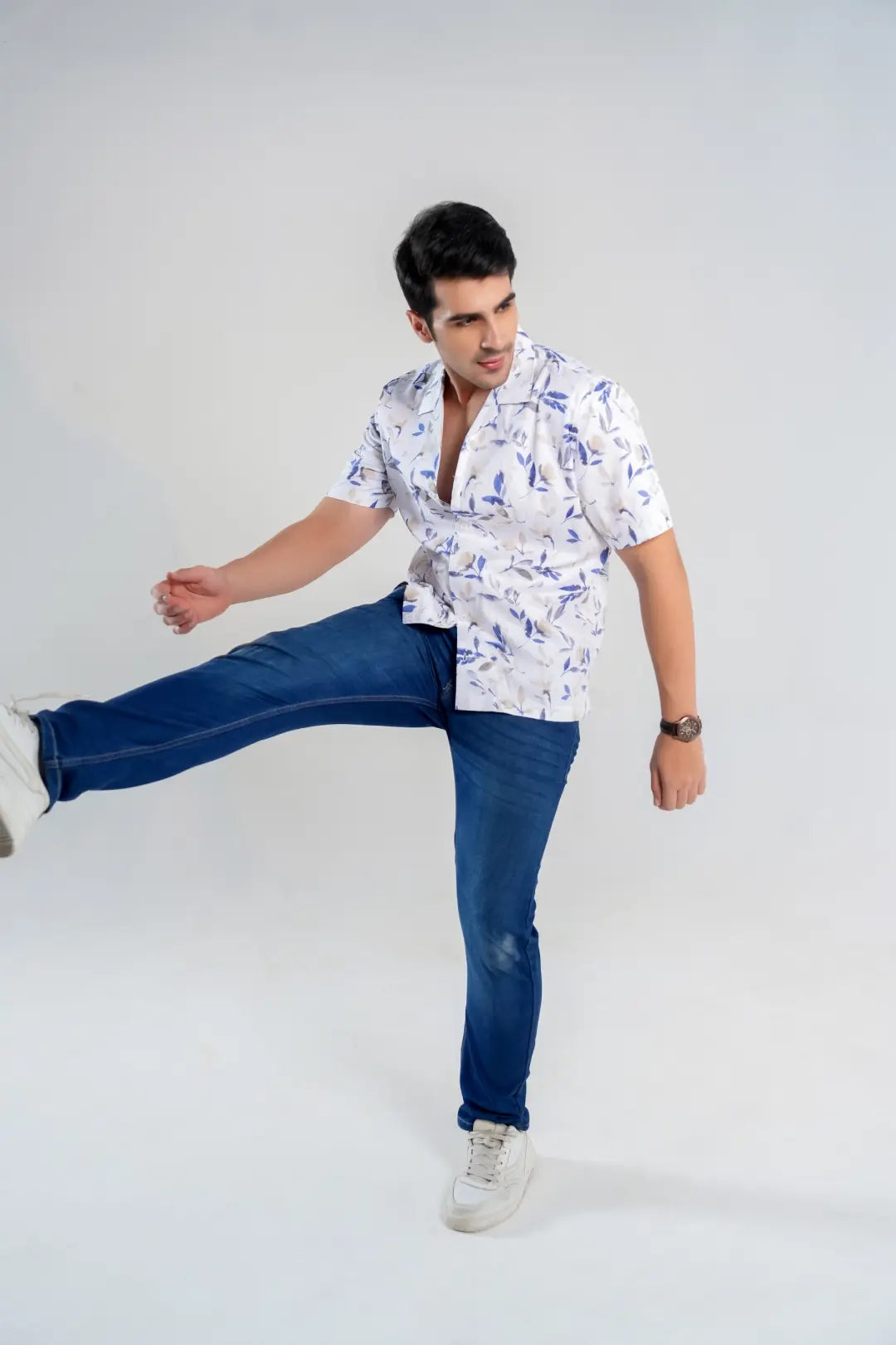 Man wearing a patterned shirt and blue jeans posing against a white background
