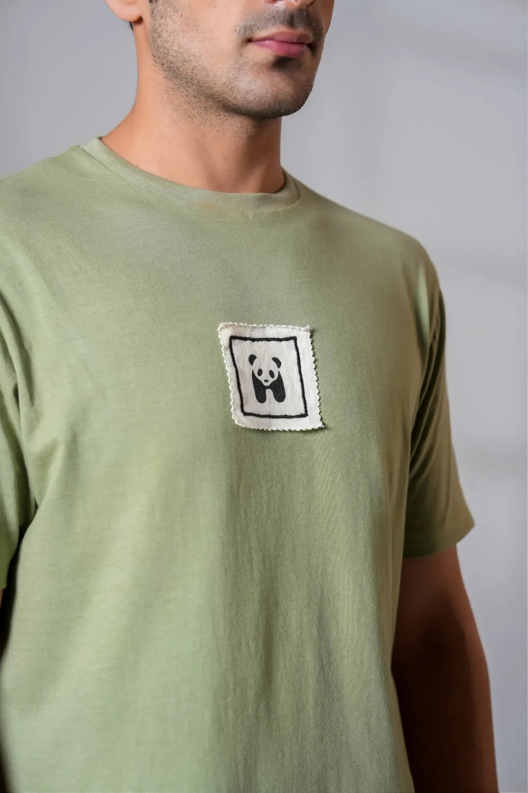 Close-up of male chest wearing olive green t-shirt with a stitched panda patch, showing soft cotton fabric texture and minimalist design detail