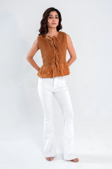 Woman wearing brown sleeveless top with smocked bodice, tie-front closure, and flowy peplum hem – front view