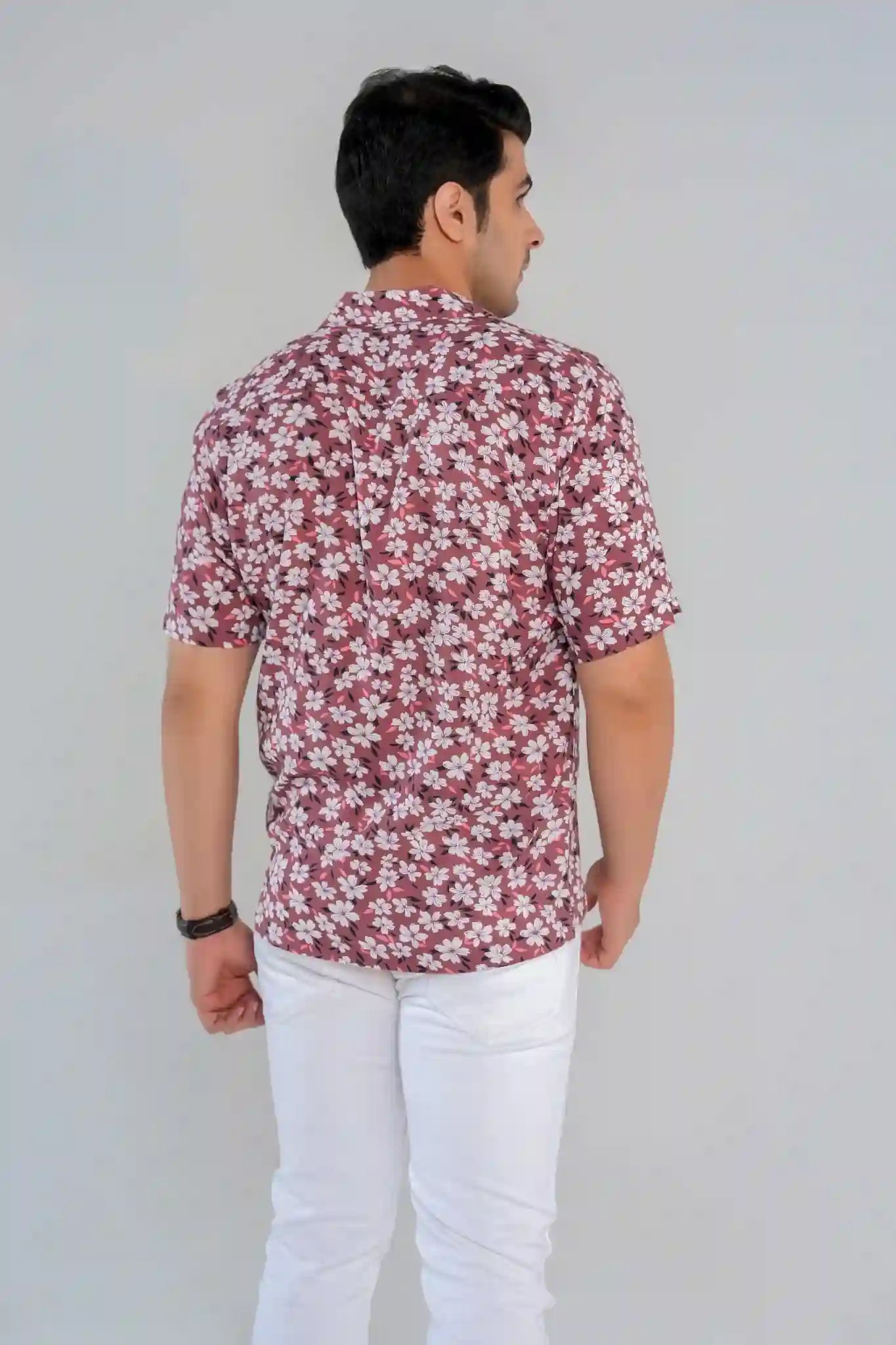 Rear view of a man wearing a rust floral printed shirt with short sleeves and white pants, highlighting back cut and fabric flow