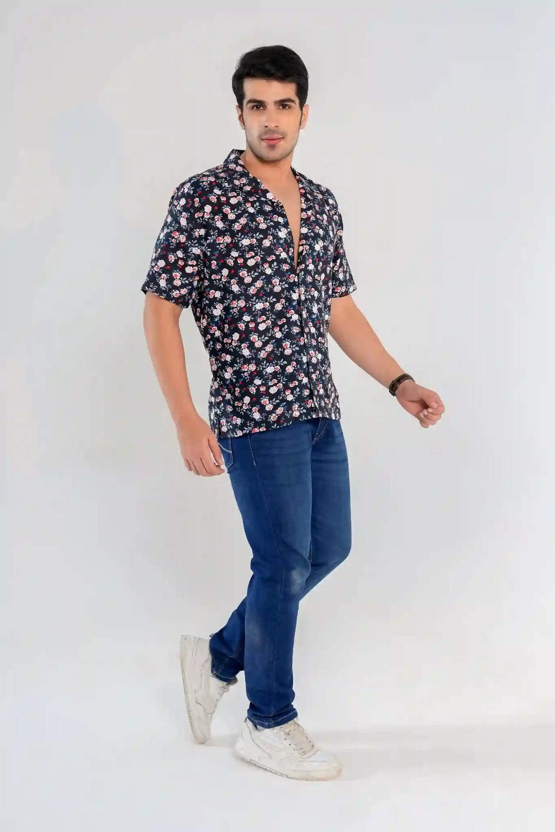 Close-up of a man adjusting the collar of a navy floral shirt paired with denim jeans, showcasing casual summer styling