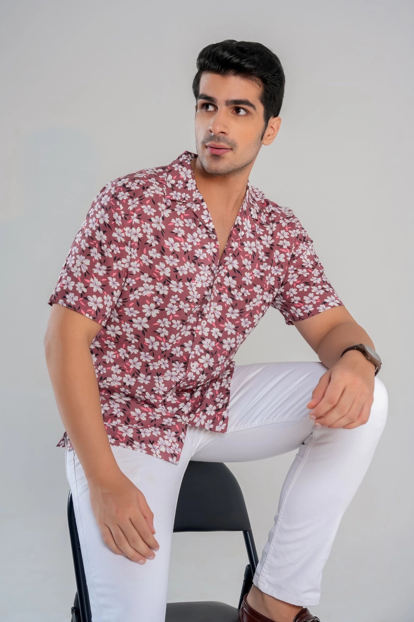 Man seated on a chair wearing a rust floral cotton-viscose shirt and white jeans, styled for a casual summer look