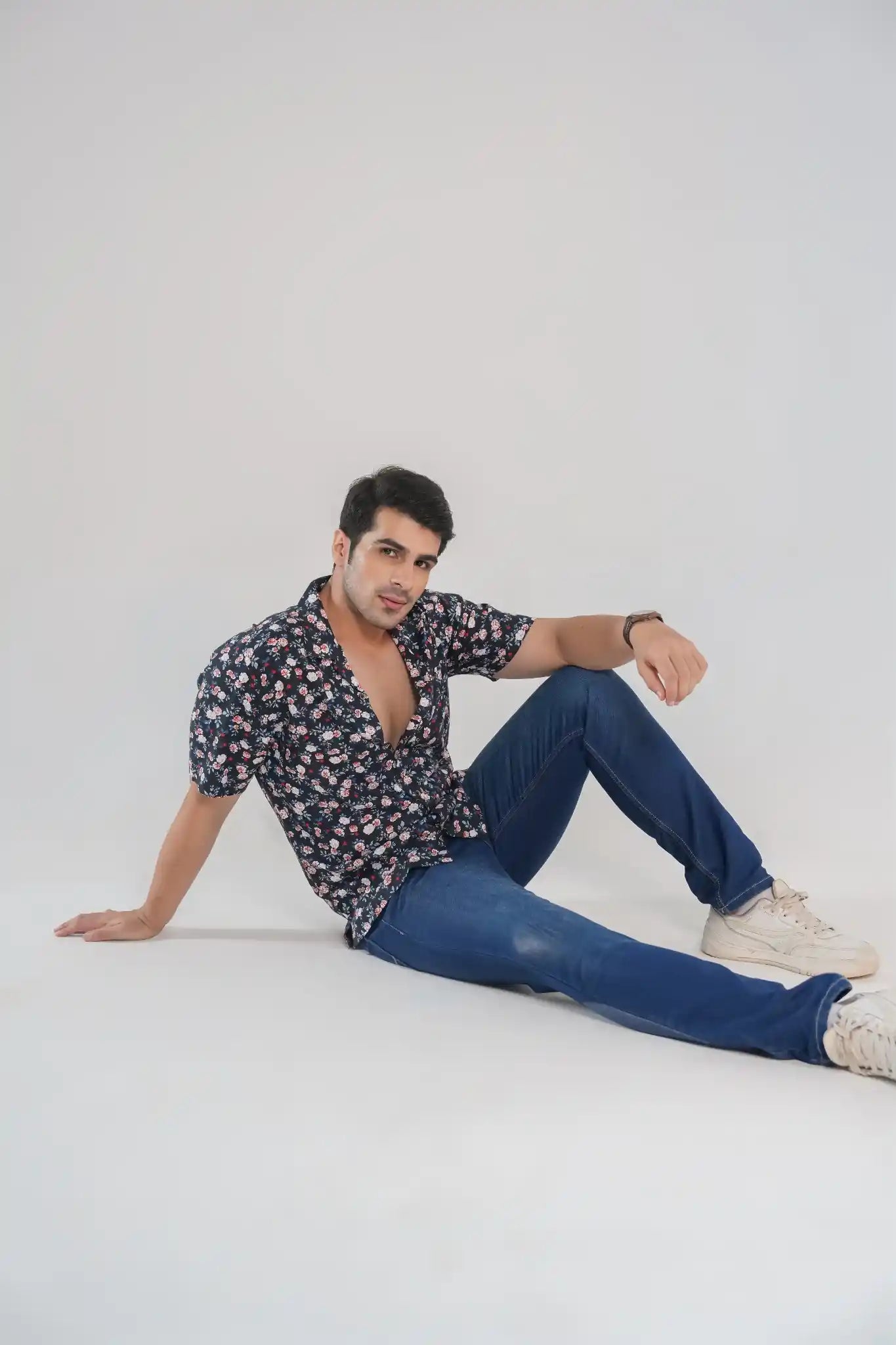Man lounging on the floor in a navy floral Cuban collar shirt with jeans and sneakers, styled for modern casualwear