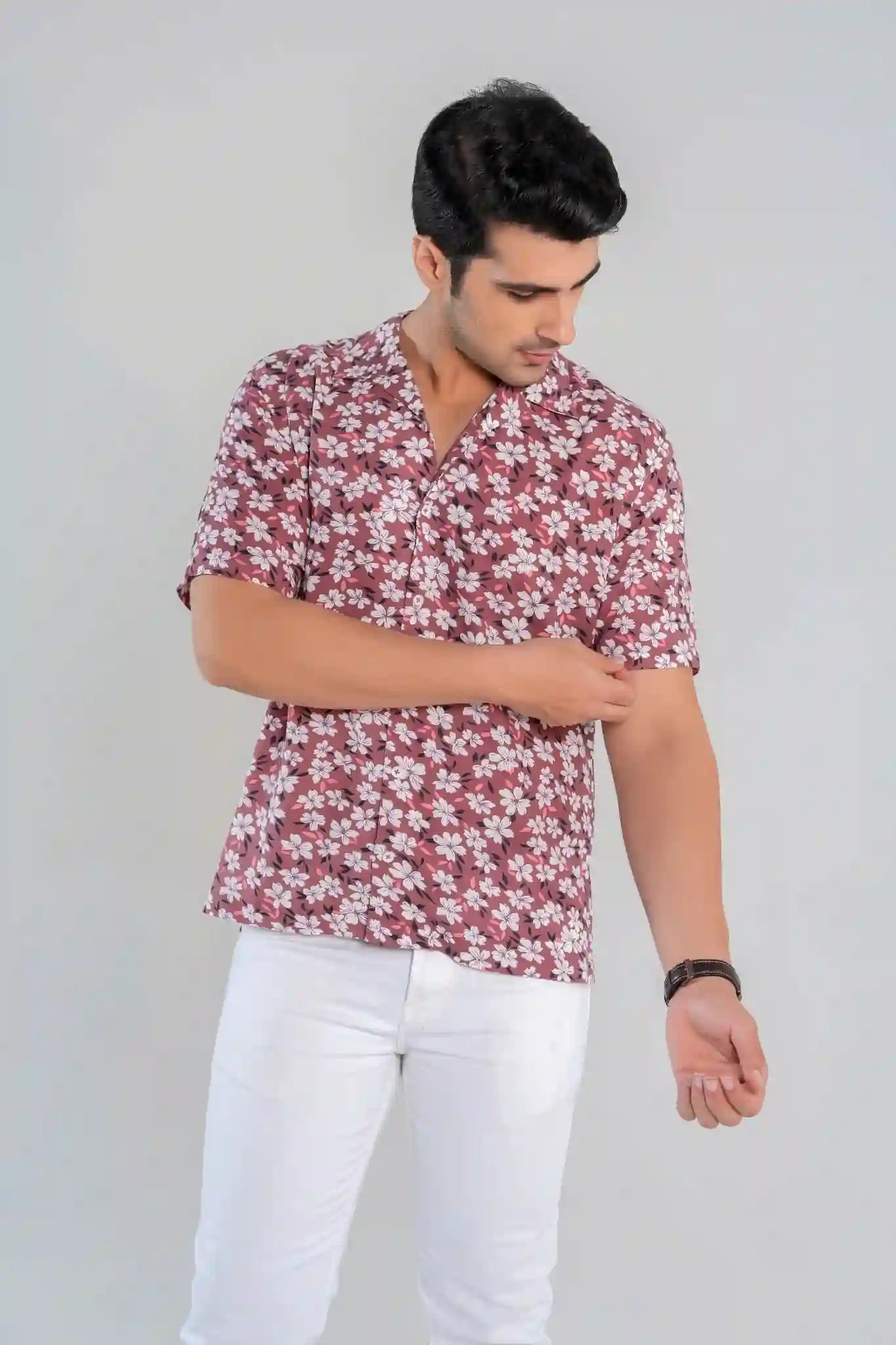 Male model posing in a rust floral button-down shirt and white trousers under soft lighting, showcasing summer-ready outfit